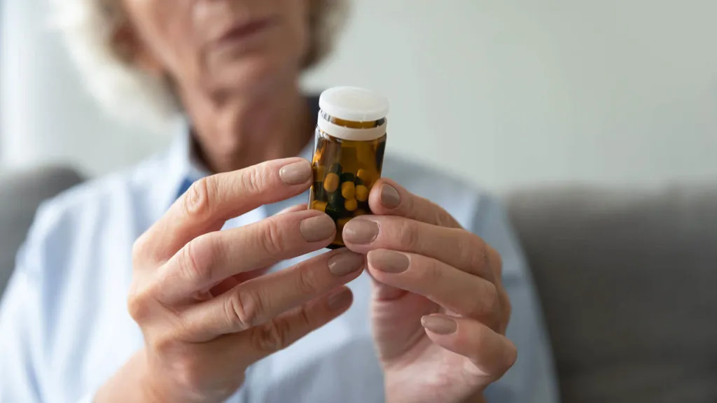 Senior woman holding prescription medication bottle at home