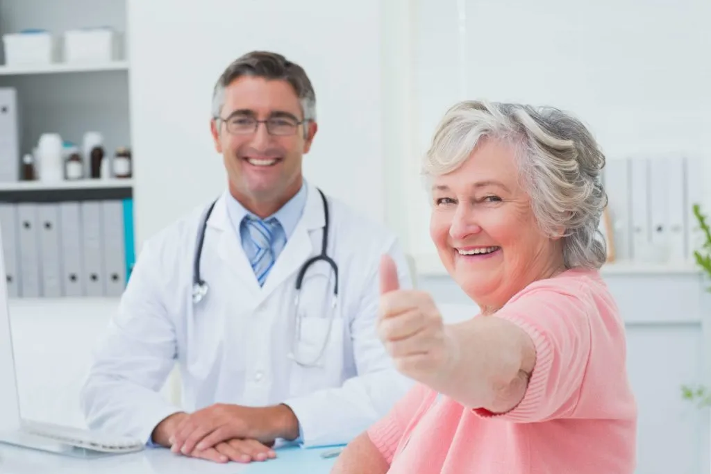 Smiling senior patient giving thumbs up during doctor consultation