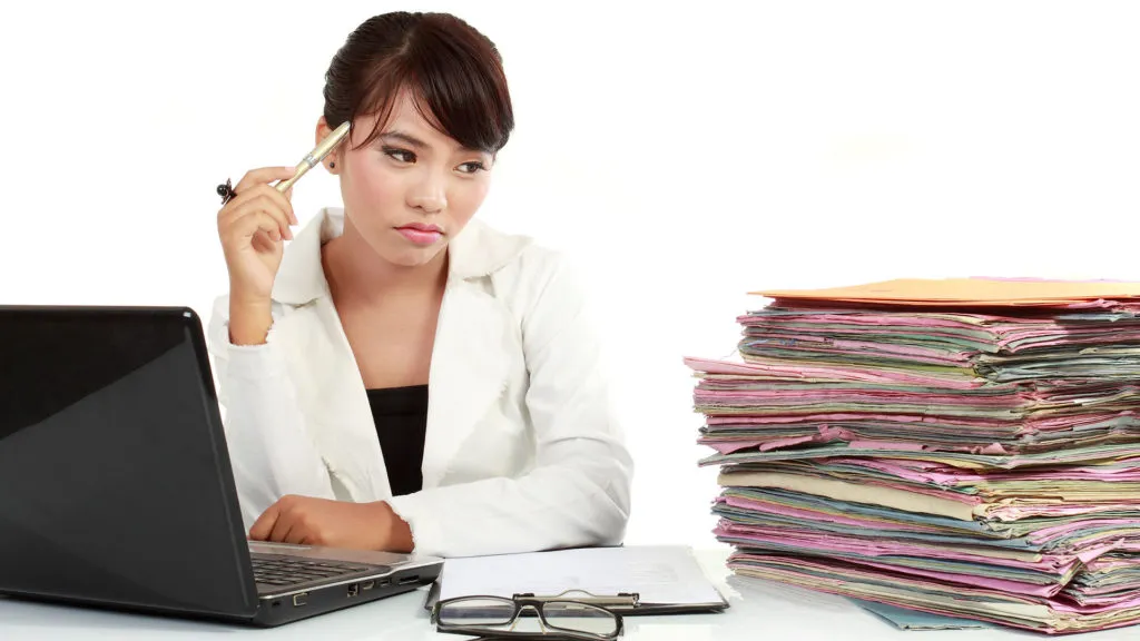 Stressed medical office worker with paperwork and laptop at desk