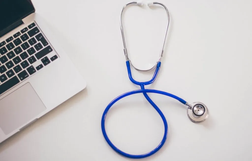 Blue stethoscope beside laptop computer on white desk