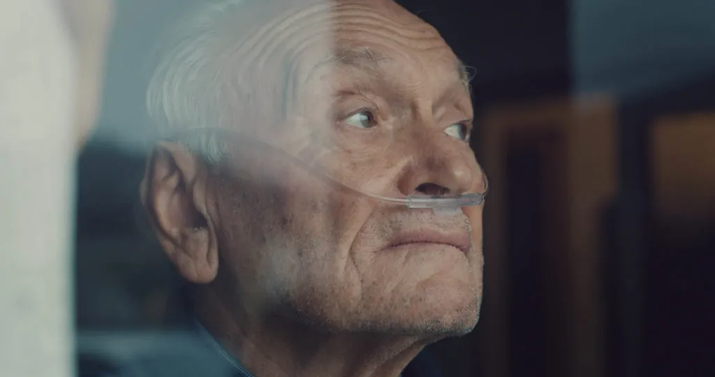 Elderly man wearing oxygen nasal cannula looking through window