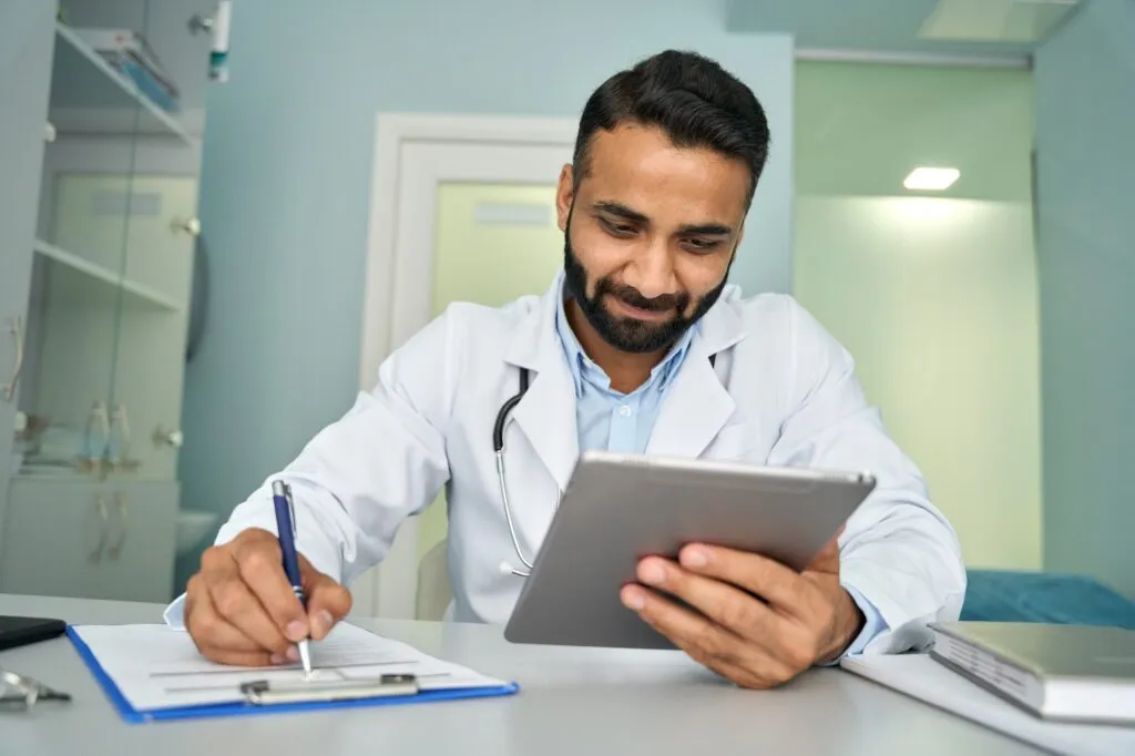 Doctor using tablet and writing medical notes in clinic